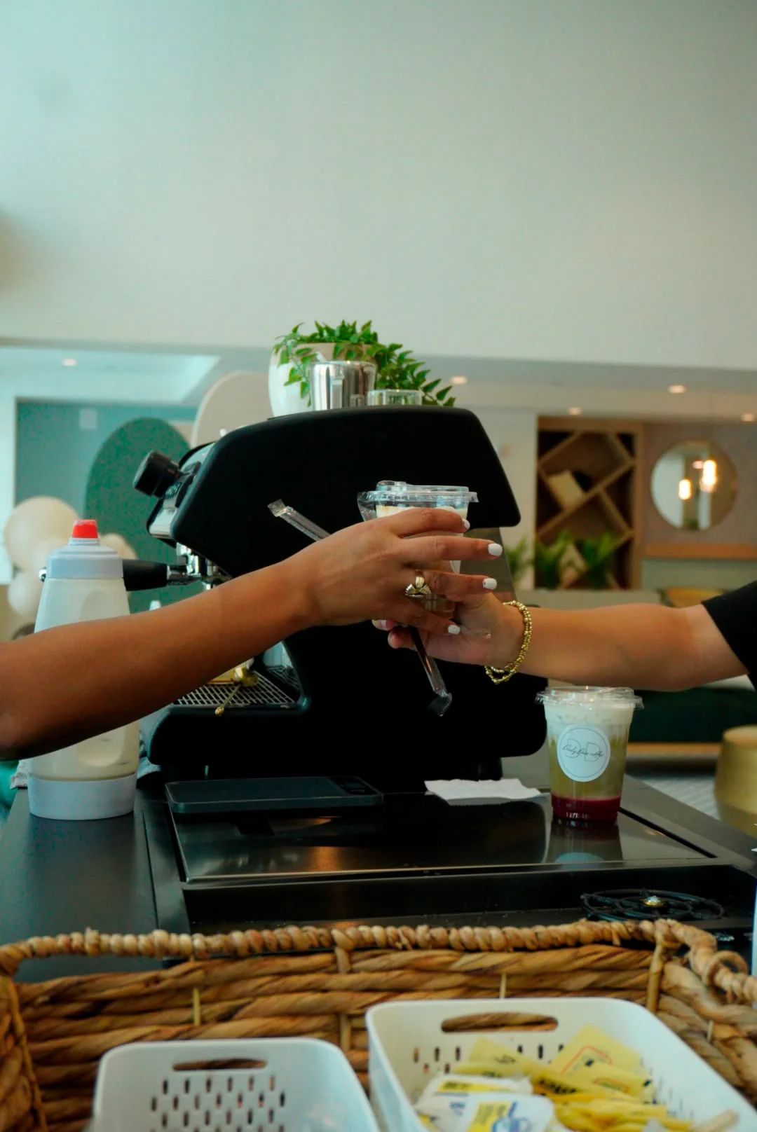 A barista hands a guest an iced drink across the espresso machine; a layered strawberry matcha with the Daily Dose sticker sits on the bar